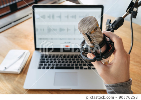 Man's hand holding a microphone on home studio podcast background Man's hand holding a microphone on home studio podcast background 90576258