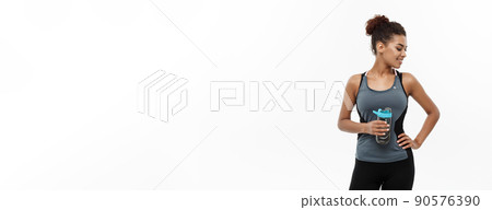 Healthy and Fitness concept - beautiful African American girl in sport clothes holding water bottle after workout. Isolated on white studio background Healthy and Fitness concept - beautiful African American girl in sport clothes holding water bottle after workout. Isolated on white studio background 90576390