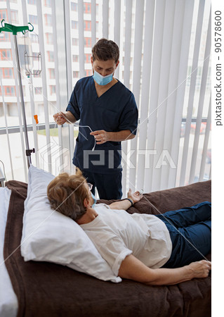 Doctor putting a drip on the arm of her patient in mask during pandemic of Covid 19 Doctor putting a drip on the arm of her patient in mask during pandemic of Covid 19 90578600