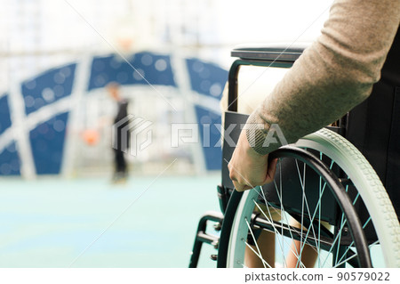 Close-up of unrecognizable disabled man in brown sweater turning in manual wheelchair while watching basketball player Close-up of unrecognizable disabled man in brown sweater turning in manual wheelchair while watching basketball player 90579022