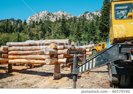 Wooden house made of round logs at the initial stage of construction and a tractor. In the background-forest, sky and mountains. Construction and structures Wooden house made of round logs at the initial stage of construction and a tractor. In the background-forest, sky and mountains. Construction and structures 90579590