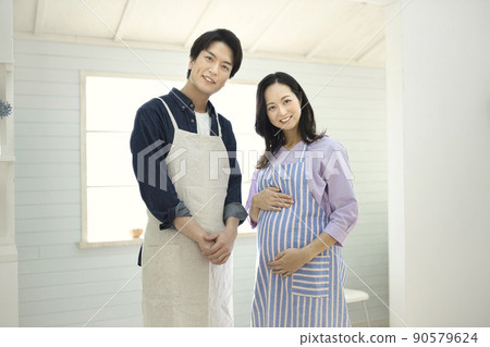 A man in an apron spending time in the kitchen with a pregnant woman 90579624