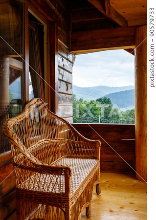 Terrace with wicker bench on wooden balcony with mountain views. 90579733