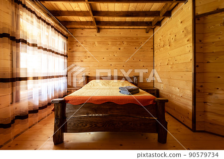 Rustic wooden bed in a cozy cottage room with a double bed, bedside table, blankets and towels. Rustic wooden bed in a cozy cottage room with a double bed, bedside table, blankets and towels. 90579734
