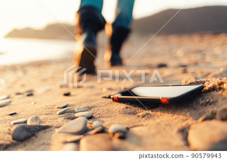 The concept of losing your phone. The smartphone lies on the sand, on the beach. In the background, blurred removing footsteps of a man 90579943