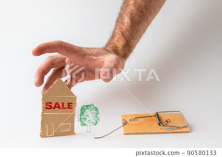 Bank investments and mortgages. Male hand reaching for the cardboard house, lying next to the trap. Text SALE. White background Bank investments and mortgages. Male hand reaching for the cardboard house, lying next to the trap. Text SALE. White background 90580133