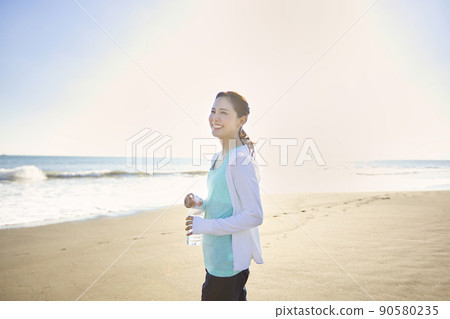 一個穿著運動服的年輕女子在沙灘上行走 90580235