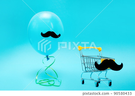 A blue balloon with mustache and a small shopping cart on a blue background. Copy space. The concept of holiday sales and Father's Day A blue balloon with mustache and a small shopping cart on a blue background. Copy space. The concept of holiday sales and Father's Day 90580433