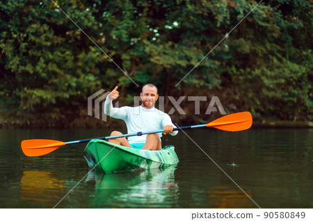 Kayaking on the river. Adult man is sitting in a kayak and gives a thumbs up. Copy space. The concept of the World Tourism Day Kayaking on the river. Adult man is sitting in a kayak and gives a thumbs up. Copy space. The concept of the World Tourism Day 90580849