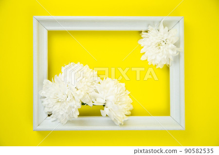 A white frame with three white flowers on a bright yellow background inside. High quality photo A white frame with three white flowers on a bright yellow background inside. High quality photo 90582535