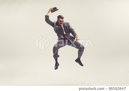 Jumping man, businessman wearing grey striped suit in 50s, 60s fashion style isolated on white background. Retro vintage style, business, ad, emotions Jumping man, businessman wearing grey striped suit in 50s, 60s fashion style isolated on white background. Retro vintage style, business, ad, emotions 90582647