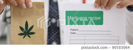 Female doctor holding marijuana recipe in one hand and package with hemp in another 90583064