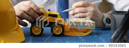 Yellow miniature toy excavator on blueprint carry wooden blocks 90583065