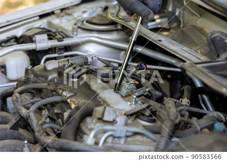 A man unscrews an old spark plug from a car engine A man unscrews an old spark plug from a car engine 90583566