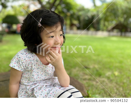 beautiful cute little girl sits and make a pose with smile in the garden with copy space 90584132