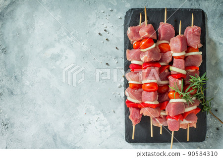 Fresh meat kebab. Meat fillet raw with cherry tomatoes, onions, spices and rosemary on a cutting board, preparation of barbecue. Copy space. Top view. Fresh meat kebab. Meat fillet raw with cherry tomatoes, onions, spices and rosemary on a cutting board, preparation of barbecue. Copy space. Top view. 90584310