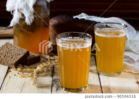 Traditional Russian cold rye drink Kvas in a glass and a jug on a wooden table. Kvass from bread, rye malt, sugar and water. Traditional Russian cold rye drink Kvas in a glass and a jug on a wooden table. Kvass from bread, rye malt, sugar and water. 90584318