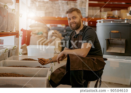 Smiling Male barista in uniform inspection freshly roasted coffee beans on manufacturing Smiling Male barista in uniform inspection freshly roasted coffee beans on manufacturing 90584610