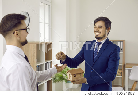 Joyful real estate man gives key to new home to young man who bought his first home. 90584898
