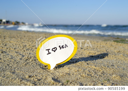 Small stick with paper speech bubble with words I love sea stands on sandy beach near sea water and sea waves with white foam close-up. Concept of travel, tourism, vacation, holiday, relax rest summer Small stick with paper speech bubble with words I love sea stands on sandy beach near sea water and sea waves with white foam close-up. Concept of travel, tourism, vacation, holiday, relax rest summer 90585199