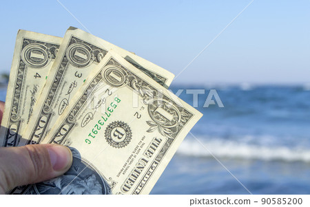 Person holds in his hand three dollar bills on the background of the waves of the blue sea. Concept money finance business tourism travel, money spending, cash expenses. Money cash expenses business Person holds in his hand three dollar bills on the background of the waves of the blue sea. Concept money finance business tourism travel, money spending, cash expenses. Money cash expenses business 90585200