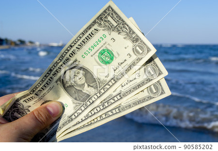Person holds in his hand three dollar bills on the background of the waves of the blue sea. Concept money finance business tourism travel, money spending, cash expenses. Money cash expenses business Person holds in his hand three dollar bills on the background of the waves of the blue sea. Concept money finance business tourism travel, money spending, cash expenses. Money cash expenses business 90585202