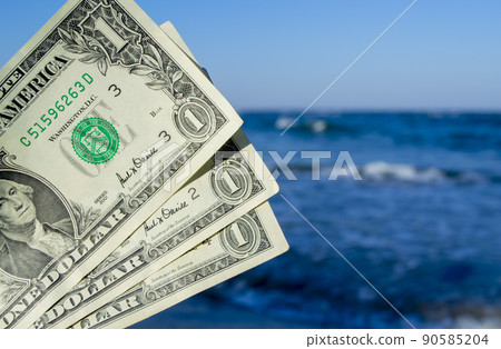 Person holds in his hand three dollar bills on the background of the waves of the blue sea. Concept money finance business tourism travel, money spending, cash expenses. Money cash expenses business Person holds in his hand three dollar bills on the background of the waves of the blue sea. Concept money finance business tourism travel, money spending, cash expenses. Money cash expenses business 90585204