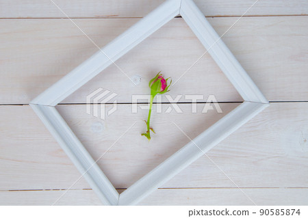 A white wooden frame lies diagonally on a white wooden background, inside it lies a bud of an unopened rose. High quality photo A white wooden frame lies diagonally on a white wooden background, inside it lies a bud of an unopened rose. High quality photo 90585874