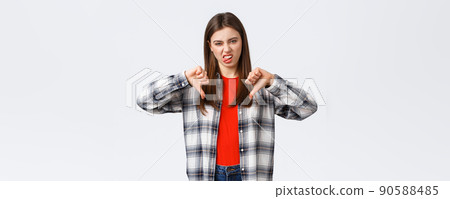 Lifestyle, different emotions, leisure activities concept. Displeased and unimpressed young picky girl in checked shirt, thumb-down and show tongue to express dislike, rate awful movie 90588485