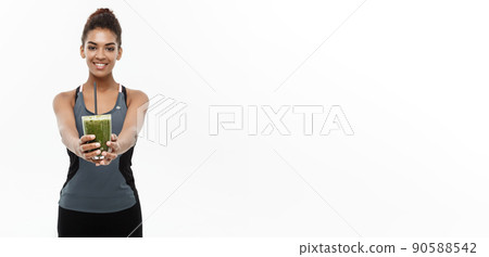Healthy and Fitness concept - Beautiful American African lady in fitness clothing drinking healthy vegetable drink. Isolated on white background. Healthy and Fitness concept - Beautiful American African lady in fitness clothing drinking healthy vegetable drink. Isolated on white background. 90588542
