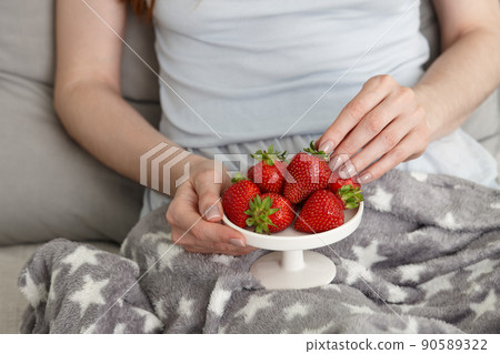 Young woman eating fresh strawberries in bed for breakfast Young woman eating fresh strawberries in bed for breakfast 90589322