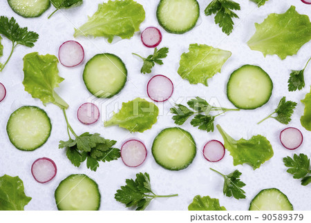 Rotating vegetable background of lettuce leaves, cucumber slices, radishes and parsley leaves on a white  90589379