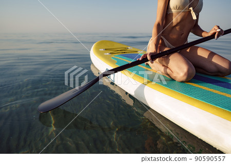 Close up of young woman sitting on a stand up paddle board Close up of young woman sitting on a stand up paddle board 90590557
