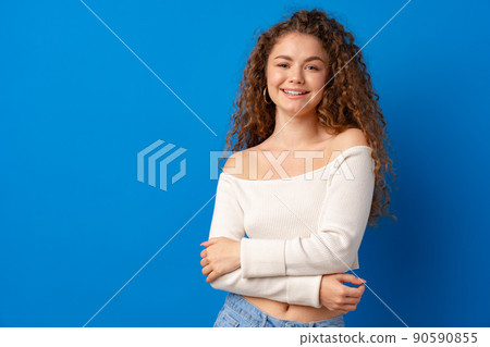 Portrait of a young attractive curly-haired woman against blue background Portrait of a young attractive curly-haired woman against blue background 90590855