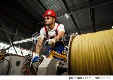 A young factory workman rolls heavy coil of electric cable 90590937