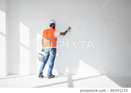 Plasterer in workwear smoothing wall surface of building indoors 90591235