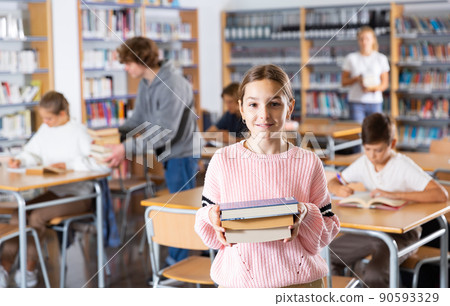 Preteen girl standing with a stack of books inlibrary Preteen girl standing with a stack of books inlibrary 90593329