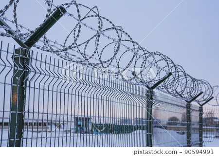 Fence with barbed wire covered with snow in the evening. 90594991