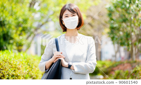 A business woman in a mask stands against the background of fresh green 90601540