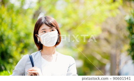 A business woman in a mask stands against the background of fresh green 90601541