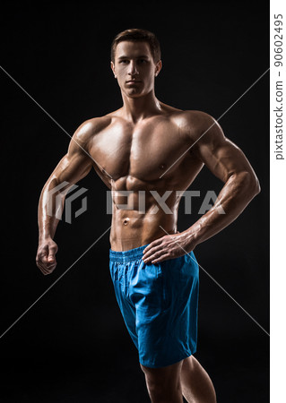 Muscular and fit young bodybuilder fitness male model posing over black background. Muscular and fit young bodybuilder fitness male model posing over black background. 90602495