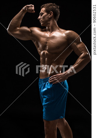 Muscular and fit young bodybuilder fitness male model posing over black background. Muscular and fit young bodybuilder fitness male model posing over black background. 90602531