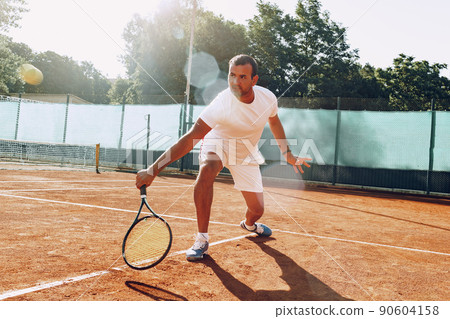 Fit man plays tennis on tennis field 90604158
