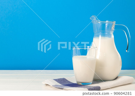 Glass and pitcher of milk against blue background Glass and pitcher of milk against blue background 90604281