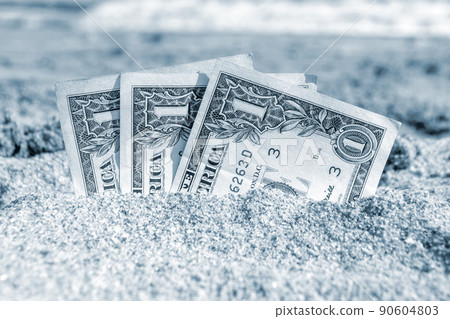 Three paper cash one dollar bills half buried in the sand on the seashore close-up. Concept money, business, savings, financial, investment, cash. Blue color 90604803