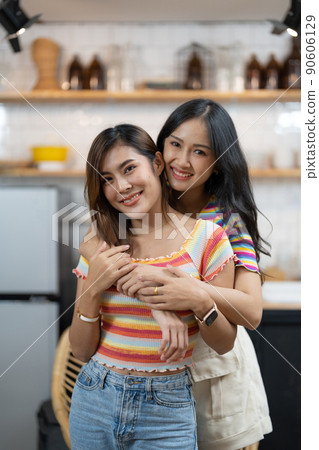 Smiling young asian lesbian couple standing affectionately together at home 90606129