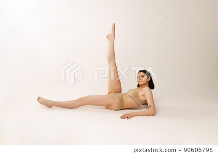 Portrait of young beautiful woman, lying on floor, posing in underwear isolated over grey studio background Portrait of young beautiful woman, lying on floor, posing in underwear isolated over grey studio background 90606798