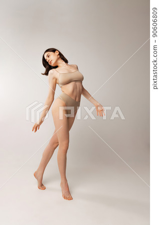 Portrait of beautiful young woman posing in beige underwear isolated over grey studio background. Natural beauty Portrait of beautiful young woman posing in beige underwear isolated over grey studio background. Natural beauty 90606809