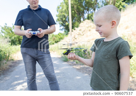 Dad and child playing with radio-controlled helicopter. Blond boy holds in his hand a mini-model of a helicopter in which propellers work. Kid develops fine motor skills. Happy childhood and love 90607537
