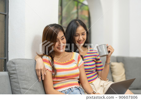 Lesbian couple sitting on sofa together and using laptop computer. 90607806